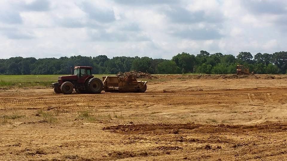 Tractor pulling a land plane across a cleared field with a dozer working in the background
