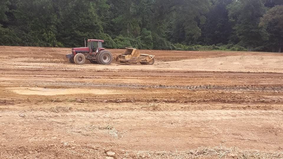Farm tractor towing a land plane to level dirt on a construction site