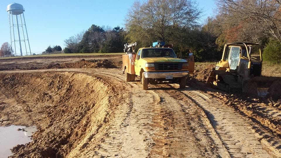 Excavation crew working near a pond site with the Canton water tower in the background
